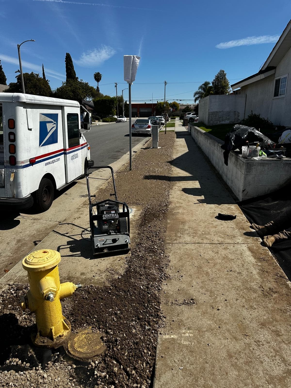 USPS truck parked on a residential street near a yellow fire hydrant and construction equipment.
