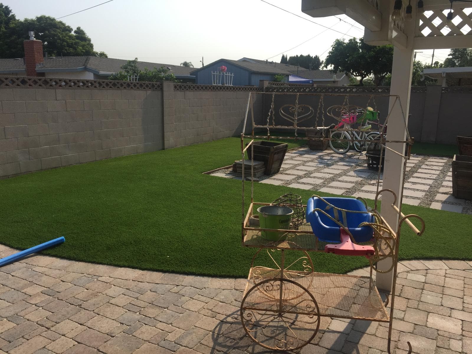 Backyard featuring artificial turf, stone pavers, a decorative metal cart, and a block wall.